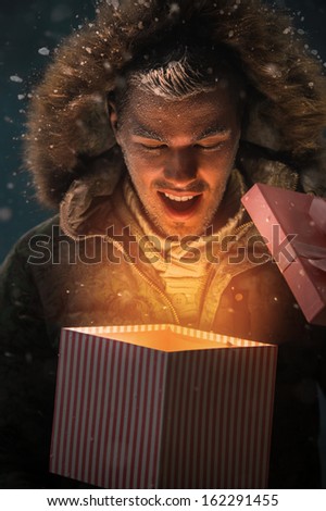 Happy Young Man Opening a Gift Box Outdoors at Night on Christmas Eve