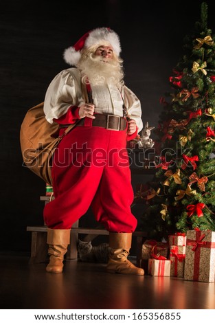 Full length portrait of Real Santa Claus carrying big bag full of gifts, at home near Christmas Tree
