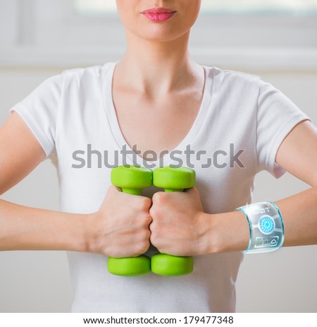 Portrait of pretty young woman wearing smart watch device while lifting dumbbells