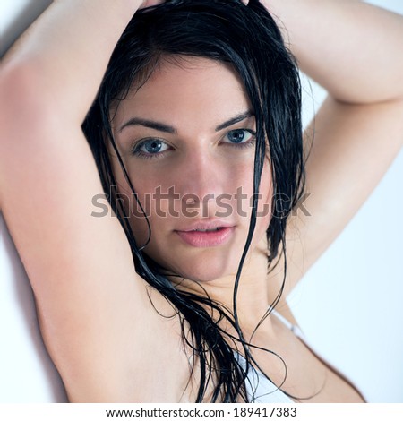 Beautiful young woman with wet hair leaning on white wall after shower in bathroom