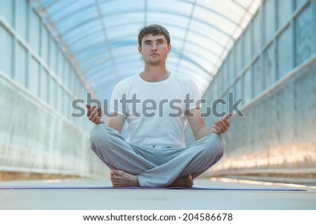 Full length of a young man meditating in lotus position outdoors at bridge