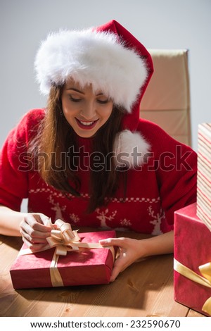 Young pretty woman wearing Santa Claus hat wrapping Christmas gift at her desk