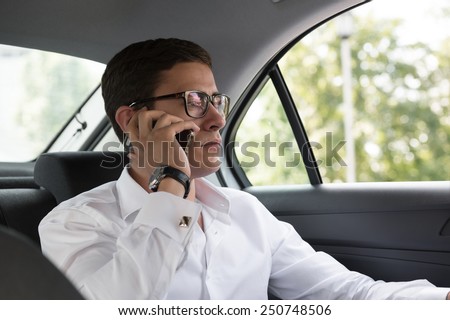 Business talk in car. Confident young businessman talking on the mobile phone and looking away while sitting on the back seat of a car
