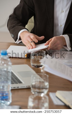 Image of male hands leafing through book or notepad during discussion at meeting