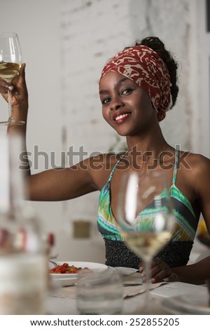 African woman eating at home and drinking wine and looking very happy