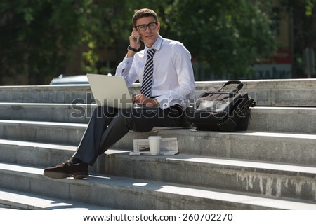 Man with laptop calling by phone at summer park on bright day
