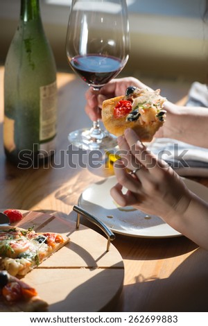 Beautiful young woman eating homemade pizza and drinking red wine at home