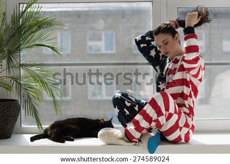 Young woman wearing American Flag pajamas celebrating Independence Day with her cat at home
