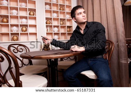 Portrait of young, handsome man thinking and waiting for woman in cafe