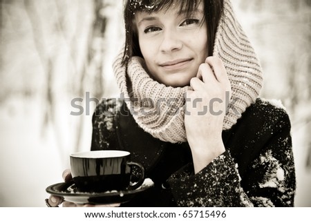 Closeup portrait of european style fashionable brunette woman drinking coffee in winter forest with snow on her hair