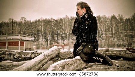 Portrait of young beautiful woman - sitting on dead tree on seaside cold and waiting for someone. Loneliness concept