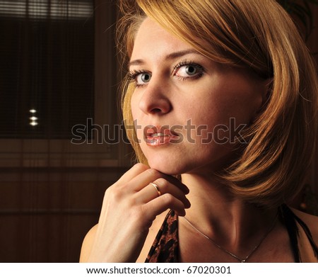 Portrait of a calm young woman sitting inside dark room with romantic light