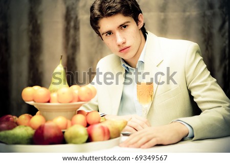 Portrait of young rich man sitting alone in his apartment drinking champagne and eating fresh fruits