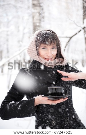 Young attractive woman outdoor in winter park holding cup in her arms and drinking warm drink.