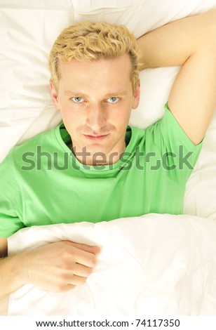 Attractive man relaxing in bed. White silk linen