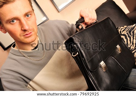 Happy young man sitting on sofa at home and holding handbag