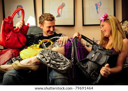 Smiling fashionable rich attractive couple sitting on sofa at home laying under lots of handbags