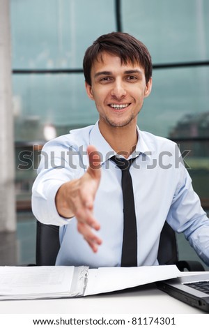 Happy mature business man offering a welcoming hand sitting at his desk. Vertical shot