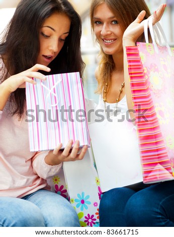 Two excited shopping woman resting on bench at shopping mall. Looking into shopping bags