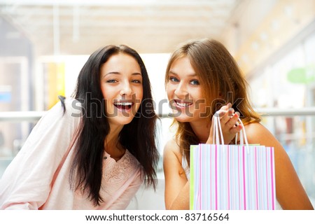 Two excited shopping woman together inside shopping mall laughing and gossip. Horizontal Shot