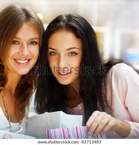 Two excited shopping woman resting on bench at shopping mall looking at camera