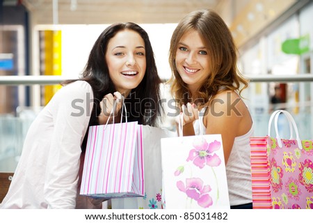Two excited shopping woman together inside shopping mall laughing and gossip. Horizontal Shot