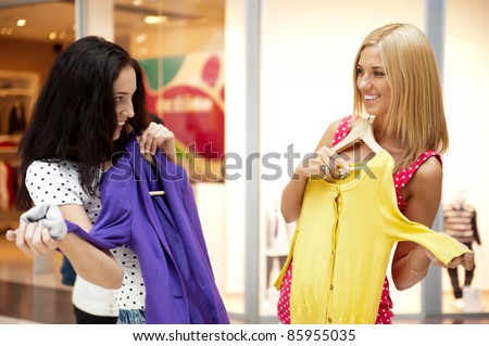 Group of two beautiful shopping women trying on clothes at shopping mall indoors