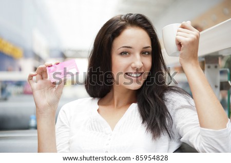 Closeup portrait of a pretty young female having a cup of coffee and holding credit card while resting at shopping mall or tax free zone of airport