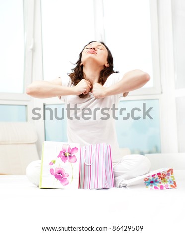 Portrait of young beautiful awake woman with gifts on bed at bedroom. She is happy and daydreaming