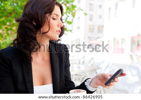 Portrait of young business woman sitting relaxed at outdoor cafe drinking coffee and chatting using her cell phone