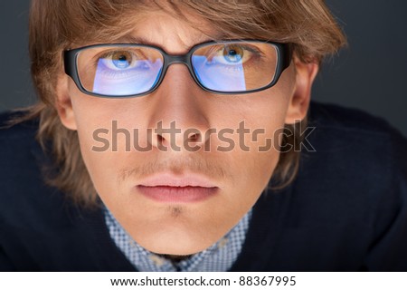 Satisfied young man with glasses looking at camera like at laptop screen, which reflects at glasses