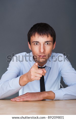 Portrait of a confident young business man in suit pointing at you while sitting at his office