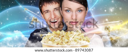 Portrait of young stylish modern couple watching movie against futuristic background embracing and eating exploding popcorn.