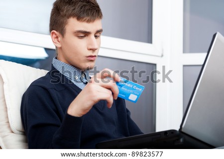 Handsome man holding credit card and using laptop for online shopping - indoors