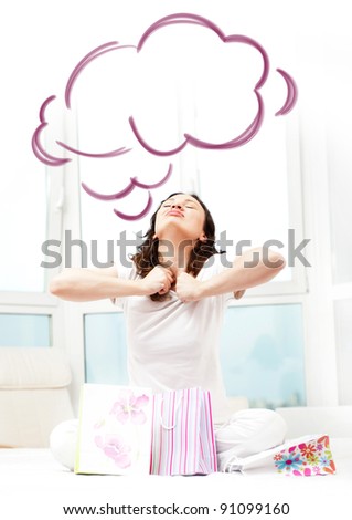 Portrait of young beautiful awake woman with gifts on bed at bedroom. She is happy and daydreaming. Blank cloud balloon overhead