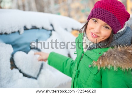 Beauty woman in the winter clothes drawing heart on car
