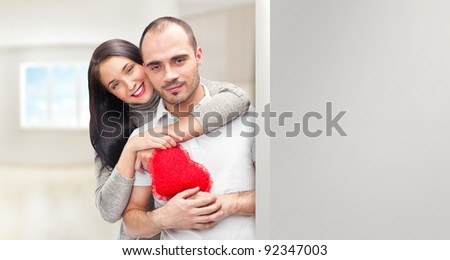 Portrait of young couple with red heart standing at their home and embracing. They are really happy to be together. Lots of copyspace for your needs