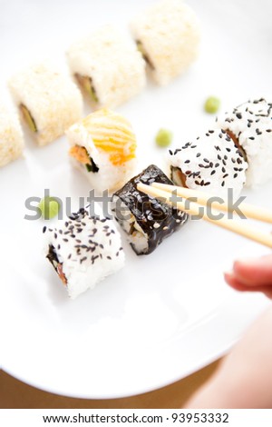 Sushi rolls on white plate and arm with chopsticks