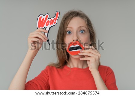 Beautiful girl wondering and surprised portrait - holding fake paper mouth and wow sign