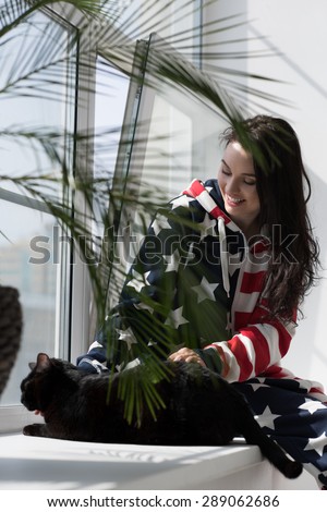Young woman wearing American Flag pajamas celebrating Independence Day with her cat at home