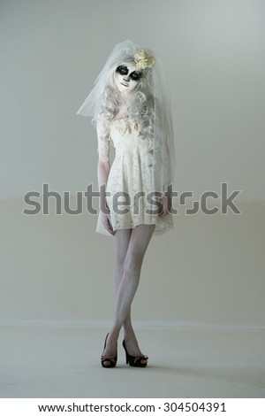 Halloween witch. Beautiful woman wearing santa muerte mask and wedding dress posing full length
