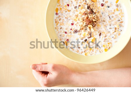 Cereal muesli breakfast with dried fruit and nuts and milk and woman hands on table. Top View