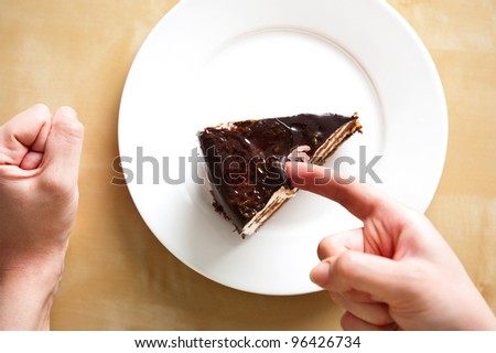 Delicious french chocolate cake on white plate on table. Woman arms near it. Top view. Sweet breakfast.