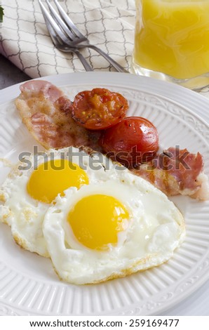 Breakfast with fried eggs, bacon, grilled tomato and orange juice.