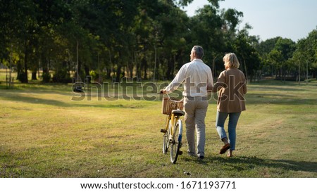 Caucasian elderly couples walking with a bicycle in the natural autumn sunlight garden feel cherish and love, concept elderly love, warm family, Happier Old-Age, retirement lifestyle.