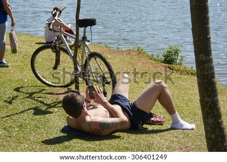 SAO PAULO, BRAZIL - August 2: Person in Ibirapuera Park in late sunny week, lying down and resting, close to other people in the city of Sao Paulo, on August 2, 2015.