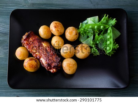Gourmet Main Dish with roast pork ribs and fried potatoes on a black plate. Served on a wooden table.