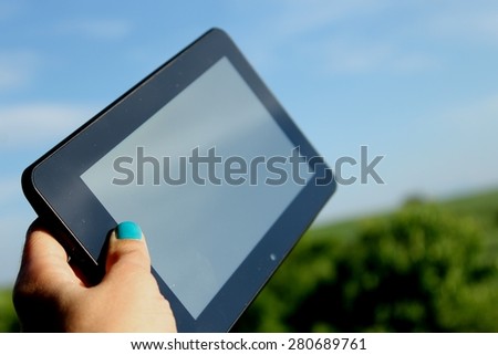 Woman\'s hand holds touchscreen tablet computer and nature in background - unique perspective