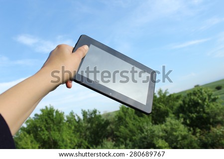 Woman\'s hand holds touchscreen tablet computer and nature in background - unique perspective