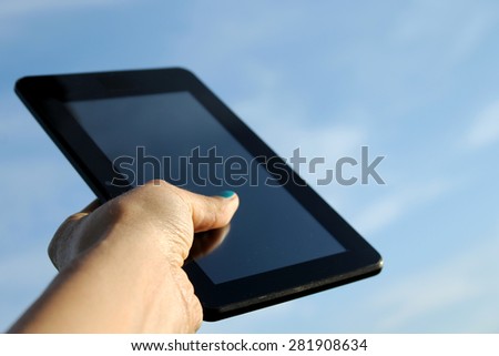 Woman\'s hand holds touchscreen tablet computer and the sky is in background - unique perspective